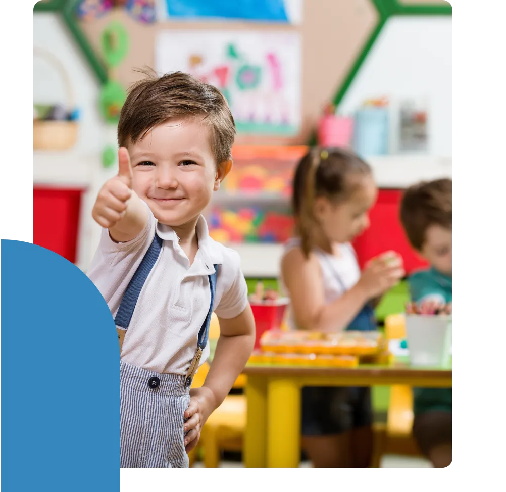 A little boy in suspenders looks at the camera, smiling, and gives a thumbs up.